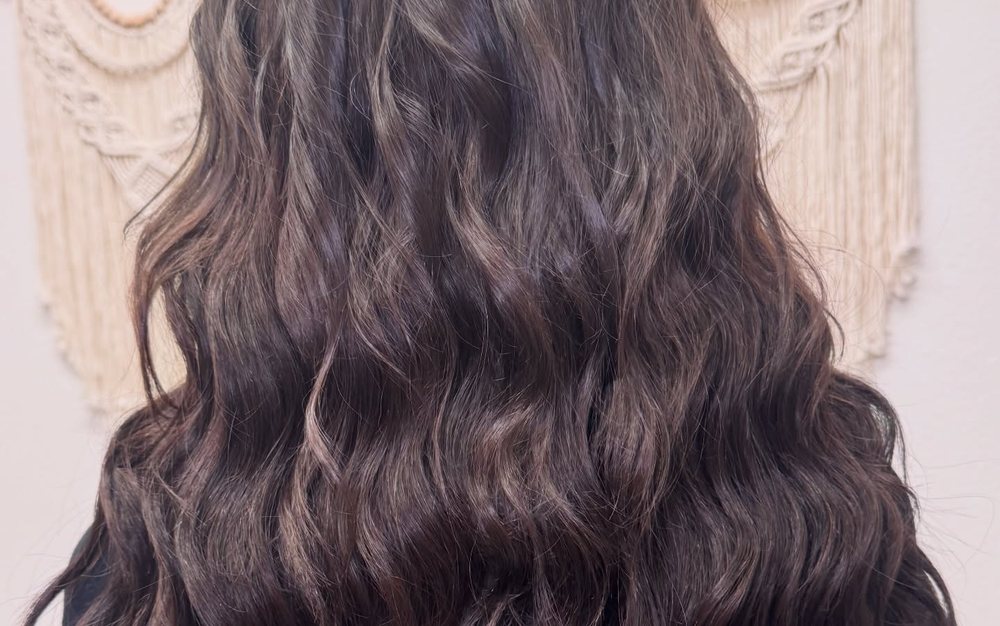 Long, full dark waves after a sew-in weft extension install by an extension-certified stylist.